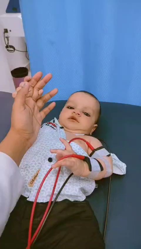 An infant lying on a clinic treatment surface with an adult's hand nearby